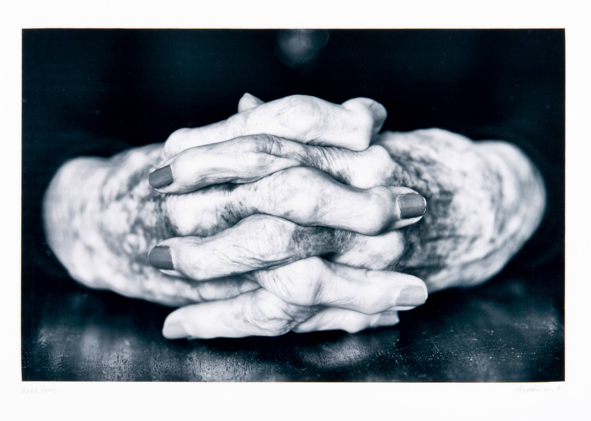 Black and white photograph of clasped women's hands. Background is black.